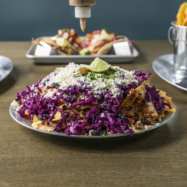 Vida Taco Bar's nachos with purple cabbage, cheese, and black beans, with sauce drizzling.