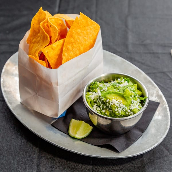 Vida Taco Bar's guacamole with cotija cheese and cilantro, served with tortilla chips and a lime wedge.