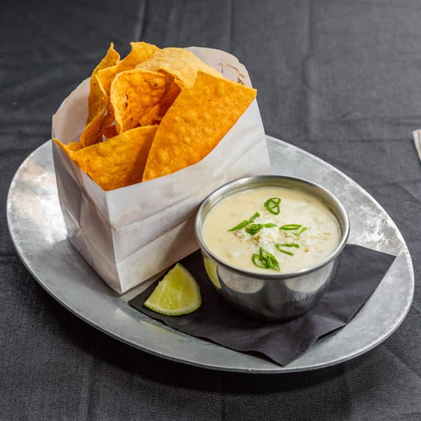 Vida Taco Bar's queso dip with crumbled cheese, green onions, and tortilla chips in a paper bag.