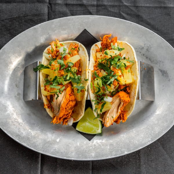 Two Vida Taco Bar tacos with red meat, pineapple, and cilantro on a metal plate.