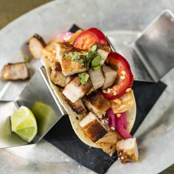 Vida Taco Bar's pork belly taco with red peppers, pickled onions, and cilantro, served with lime.
