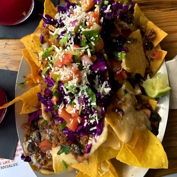 A large plate of Vida Taco Bar nachos with cheese, ground meat, red cabbage, tomatoes, and cilantro.