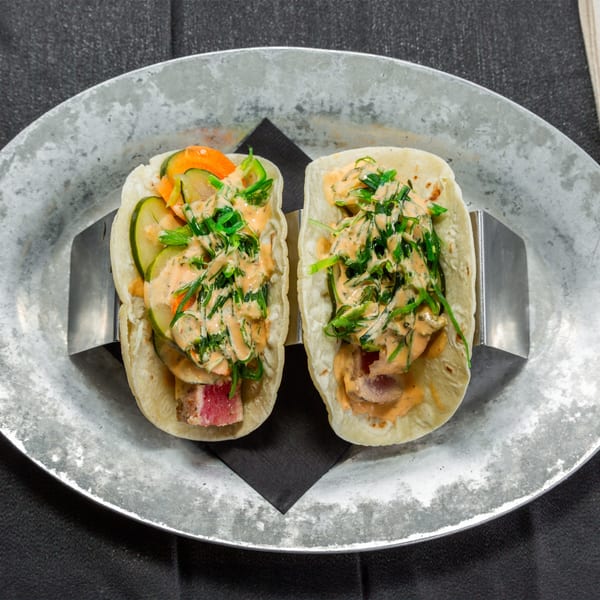 Two Vida Taco Bar tacos with tuna, vegetables, and sauce on a metal plate.