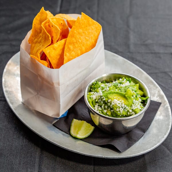 Vida Taco Bar's guacamole with cotija cheese, cilantro, and tortilla chips in a paper bag.