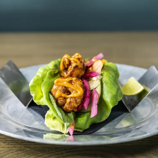 Vida Taco Bar's lettuce wrap with chicken, pickled onions, and a lime wedge on a metal plate.