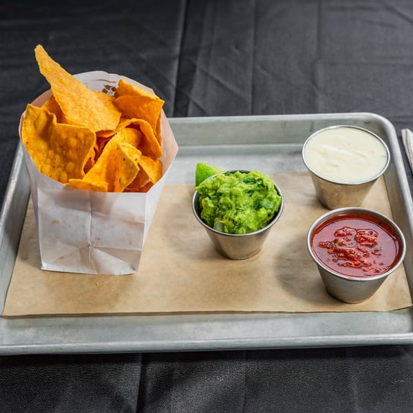 Vida Taco Bar's tortilla chips in a paper bag with guacamole, salsa, and queso on a tray.