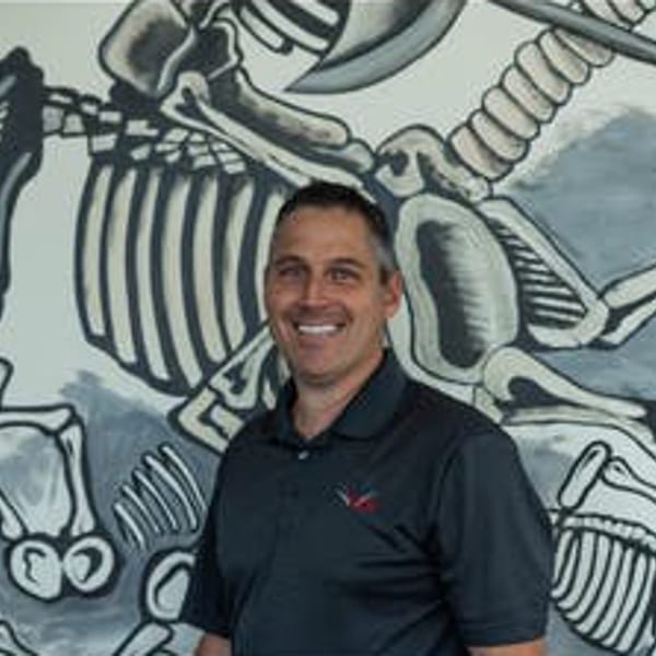 Smiling man in a dark polo shirt standing in front of a Vida Taco Bar skeleton mural.