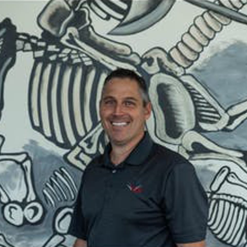 Smiling man in a dark polo shirt standing in front of a Vida Taco Bar skeleton mural.