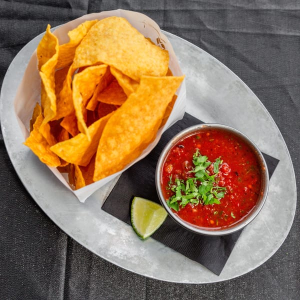 Crispy tortilla chips in a paper-lined basket with a side of red salsa and a lime wedge.