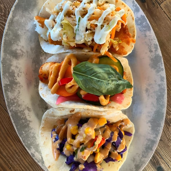 Three vibrant Vida Taco Bar tacos, each with unique fillings and sauces, on a metal plate.