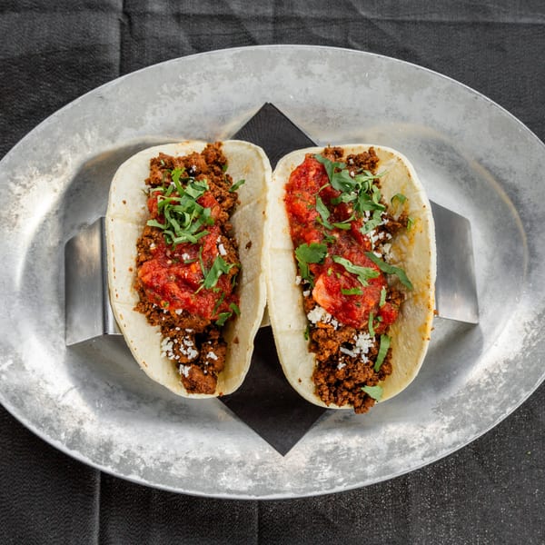 Two Vida Taco Bar tacos with ground meat, salsa, cheese, and cilantro on a metal plate.