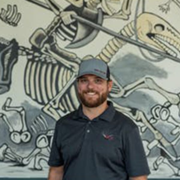 Smiling man in a hat and polo shirt standing in front of a skeleton mural at Vida Taco Bar.