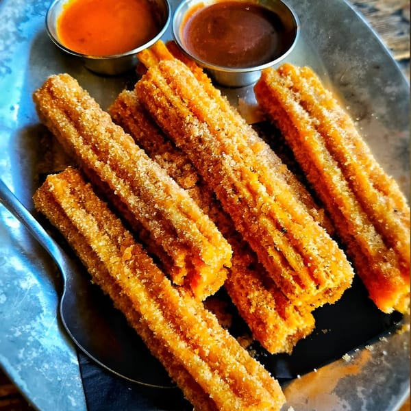 Golden churros dusted with sugar, served with two dipping sauces on a metal tray at Vida Taco Bar.