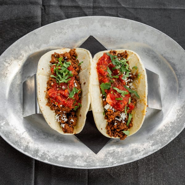 Two Vida Taco Bar tacos with ground meat, red sauce, and cilantro on a metal platter.